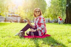 Зрелая женщина слушая к музыке на наушниках Сидит на траве в парке, отдыхая наслаждает природой Стоковые Изображения Зрелая женщина слушая к музыке на наушниках Сидит на траве в парке, отдыхая наслаждает природой Стоковые Изображения