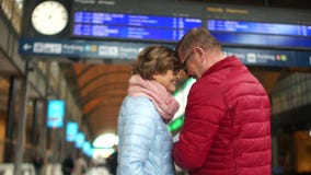 Зрелые пары на билетах проверок железнодорожного вокзала с расписанием Человек целует женщину на лбе и они идут сток-видео Зрелые пары на билетах проверок железнодорожного вокзала с расписанием Человек целует женщину на лбе и они идут сток-видео