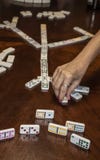 Игра домино когтя цыпленка с рукой играя плитку и показывая людям одному части игры с отражениями в деревянном столе стоковые фото Игра домино когтя цыпленка с рукой играя плитку и показывая людям одному части игры с отражениями в деревянном столе стоковые фото