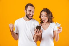 Изображение добросердечных человека и женщины пар используя сотовый телефон и кредитную карточку, изолированное над желтой предпо стоковое изображение Изображение добросердечных человека и женщины пар используя сотовый телефон и кредитную карточку, изолированное над желтой предпо стоковое изображение