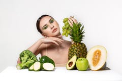 Изображение красивой молодой женщины брюнета с фруктами и овощами на таблице, держа зеленые виноградины в руке изолированный стоковые фотографии rf Изображение красивой молодой женщины брюнета с фруктами и овощами на таблице, держа зеленые виноградины в руке изолированный стоковые фотографии rf