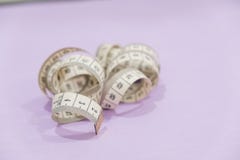 Изогнутый измерять белизны портновский метр и ножницы на фиолетовой предпосылке стоковые фото Изогнутый измерять белизны портновский метр и ножницы на фиолетовой предпосылке стоковые фото