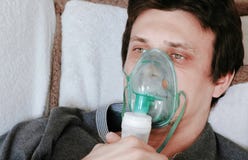 Используйте nebulizer и ингалятор для обработки Сторона ` s молодого человека вдыхая через маску ингалятора лежа на кресле сторон стоковые изображения Используйте nebulizer и ингалятор для обработки Сторона ` s молодого человека вдыхая через маску ингалятора лежа на кресле сторон стоковые изображения