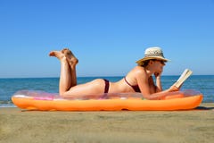 Кавказская девушка при шляпа лежа на раздувном тюфяке и читая книгу на пляже Стоковая Фотография RF Кавказская девушка при шляпа лежа на раздувном тюфяке и читая книгу на пляже Стоковая Фотография RF