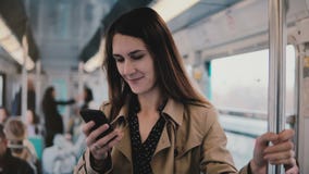 Кавказская женщина используя smartphone в вагоне метро Красивые счастливые молодые новости чтения работника офиса от передвижного акции видеоматериалы Кавказская женщина используя smartphone в вагоне метро Красивые счастливые молодые новости чтения работника офиса от передвижного акции видеоматериалы