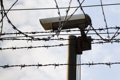Камера слежения за загородкой колючей проволоки вокруг стен тюрьмы стоковые фотографии rf Камера слежения за загородкой колючей проволоки вокруг стен тюрьмы стоковые фотографии rf