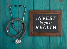 Классн классный с текстом & x22; Проинвестируйте в вашем health& x22; и стетоскоп на голубой деревянной предпосылке стоковые фотографии rf Классн классный с текстом & x22; Проинвестируйте в вашем health& x22; и стетоскоп на голубой деревянной предпосылке стоковые фотографии rf