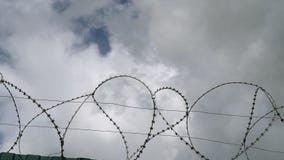 Колючая проволока против голубого неба с белыми облаками Колючая проволока против голубого неба с белыми облаками