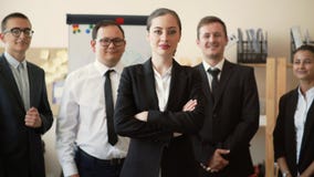 Коммерсантка стоит в офисе с ее оружиями пересекла, ее работники стоит за ей и улыбкой, teambuild видеоматериал Коммерсантка стоит в офисе с ее оружиями пересекла, ее работники стоит за ей и улыбкой, teambuild видеоматериал