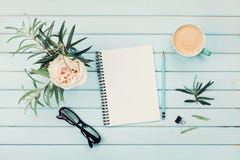 Кофейная чашка утра, чистая тетрадь, карандаш, eyeglasses и цветок года сбора винограда розовый в вазе на голубом деревенском взг Кофейная чашка утра, чистая тетрадь, карандаш, eyeglasses и цветок года сбора винограда розовый в вазе на голубом деревенском взг