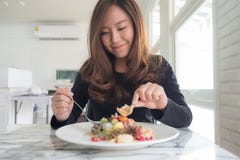 Красивая азиатская женщина наслаждается съесть фруктовый салат на таблице в ресторане стоковое фото rf Красивая азиатская женщина наслаждается съесть фруктовый салат на таблице в ресторане стоковое фото rf