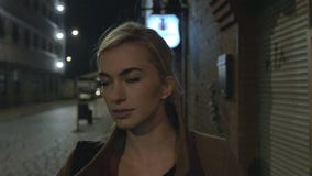 Красивая белокурая женщина в outdoors пальто идя одном на ноче зерно движение медленное Красивая белокурая женщина в outdoors пальто идя одном на ноче зерно движение медленное