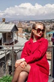 Красивая блондинка маленькой девочки в солнечных очках и красном пальто, стойках на предпосылке города Тбилиси стоковые изображения Красивая блондинка маленькой девочки в солнечных очках и красном пальто, стойках на предпосылке города Тбилиси стоковые изображения
