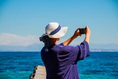 Красивая девушка в белой шляпе лета и голубой рубашке на пляже делает selfie, фото Рассказы от каникул для интернета стоковые изображения rf Красивая девушка в белой шляпе лета и голубой рубашке на пляже делает selfie, фото Рассказы от каникул для интернета стоковые изображения rf