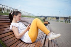 Красивая девушка сидя на стенде в парке с телефоном в руках стоковые изображения rf Красивая девушка сидя на стенде в парке с телефоном в руках стоковые изображения rf