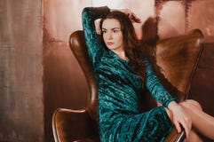 Красивая женщина в платье бархата, сидя в кожаном коричневом ch стоковые фотографии rf Красивая женщина в платье бархата, сидя в кожаном коричневом ch стоковые фотографии rf
