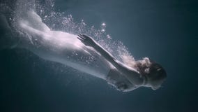 Красивая женщина плавая под водой в белом элегантном платье Красивая женщина плавая под водой в белом элегантном платье