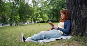 Красивая книга чтения молодой женщины сидя на одеяле под деревом в усмехаться парка акции видеоматериалы Красивая книга чтения молодой женщины сидя на одеяле под деревом в усмехаться парка акции видеоматериалы