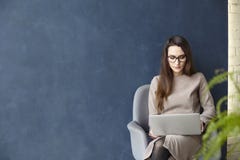 Красивая коммерсантка работая на компьтер-книжке пока сидящ в современном офисе просторной квартиры Синяя предпосылка стены, свет Стоковое Изображение RF Красивая коммерсантка работая на компьтер-книжке пока сидящ в современном офисе просторной квартиры Синяя предпосылка стены, свет Стоковое Изображение RF