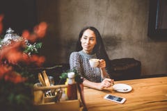 Красивая маленькая девочка выпивает кофе от белой чашки, рядом с ее сотовым телефоном в кафе украшенном с оформлением рождества стоковые изображения Красивая маленькая девочка выпивает кофе от белой чашки, рядом с ее сотовым телефоном в кафе украшенном с оформлением рождества стоковые изображения