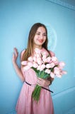 Красивая молодая женщина в розовом удерживании платья в руках скачет букет цветков тюльпанов на голубой предпосылке стены стоковые фотографии rf Красивая молодая женщина в розовом удерживании платья в руках скачет букет цветков тюльпанов на голубой предпосылке стены стоковые фотографии rf