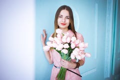 Красивая молодая женщина в розовом удерживании платья в руках скачет букет цветков тюльпанов на голубой предпосылке стены стоковые фото Красивая молодая женщина в розовом удерживании платья в руках скачет букет цветков тюльпанов на голубой предпосылке стены стоковые фото