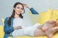 красивая молодая женщина используя ноутбук и усмехающся на камере пока сидящ на софе стоковое фото rf красивая молодая женщина используя ноутбук и усмехающся на камере пока сидящ на софе стоковое фото rf