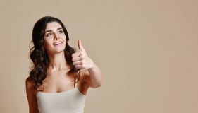 Красивая молодая женщина показывает большой палец руки вверх, держит руку на бедре, смеется и смотрится камерой стоковые изображения rf Красивая молодая женщина показывает большой палец руки вверх, держит руку на бедре, смеется и смотрится камерой стоковые изображения rf