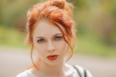 Красивая молодая женщина с красными волосами, снаружи в парке в солнечном свете, смотря в камеру стоковое фото Красивая молодая женщина с красными волосами, снаружи в парке в солнечном свете, смотря в камеру стоковое фото