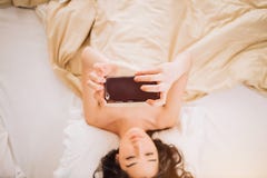 Красивая молодая усмехаясь женщина брюнета используя телефон в ее спальне стоковые фотографии rf Красивая молодая усмехаясь женщина брюнета используя телефон в ее спальне стоковые фотографии rf