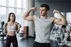Красивая пара спорт показывает их мышцы пока стоящ в спортзале стоковое фото rf Красивая пара спорт показывает их мышцы пока стоящ в спортзале стоковое фото rf