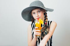 Красивая предназначенная для подростков девушка в черно-белом striped платье и круглой шляпе выпивая свежий апельсиновый сок чере стоковые фотографии rf Красивая предназначенная для подростков девушка в черно-белом striped платье и круглой шляпе выпивая свежий апельсиновый сок чере стоковые фотографии rf