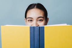 Красивая предназначенная для подростков девушка прячет ее улыбку за учебником счастливым стоковые фотографии rf Красивая предназначенная для подростков девушка прячет ее улыбку за учебником счастливым стоковые фотографии rf