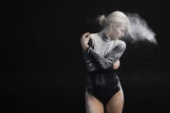 Красивая тонкая девушка нося черный гимнастический bodysuit покрытый с белым порошком обнимает и пыль летает от ее волос на a стоковые изображения Красивая тонкая девушка нося черный гимнастический bodysuit покрытый с белым порошком обнимает и пыль летает от ее волос на a стоковые изображения