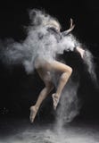 Красивая тонкая девушка нося черный гимнастический bodysuit покрытый с облаками белых скачек летая порошка танцуя на темноте стоковые изображения Красивая тонкая девушка нося черный гимнастический bodysuit покрытый с облаками белых скачек летая порошка танцуя на темноте стоковые изображения