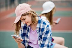 Красивая усмехаясь рубашка белокурой девушки нося checkered и крышка сидят на спортивной площадке с телефоном в ее руке стоковое фото rf Красивая усмехаясь рубашка белокурой девушки нося checkered и крышка сидят на спортивной площадке с телефоном в ее руке стоковое фото rf