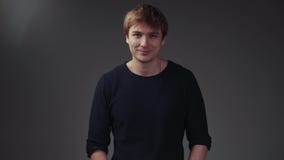 Красивый молодой европейский человек в стильном черном свитере на сером экране Смешной мальчик смотря вниз, подъемы его голова и видеоматериал Красивый молодой европейский человек в стильном черном свитере на сером экране Смешной мальчик смотря вниз, подъемы его голова и видеоматериал