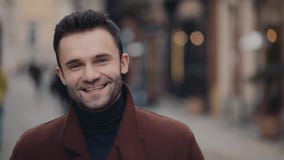 Красивый молодой человек в вскользь коричневом пальто стоя в центре города и усмехаясь ярко к камере потеха отца ребенка имея игр видеоматериал Красивый молодой человек в вскользь коричневом пальто стоя в центре города и усмехаясь ярко к камере потеха отца ребенка имея игр видеоматериал