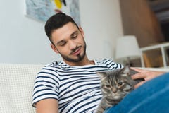 красивый молодой человек petting милый кот tabby пока сидящ стоковые фотографии rf красивый молодой человек petting милый кот tabby пока сидящ стоковые фотографии rf
