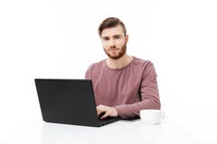 Красивый молодой человек на таблице смотря в камере работая на изолированном портативном компьютере стоковые фото Красивый молодой человек на таблице смотря в камере работая на изолированном портативном компьютере стоковые фото