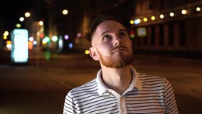 Красивый человек с бородой смотрит вверх и после этого в камере Одетый в striped рубашке и стойке поло на улице вечером акции видеоматериалы Красивый человек с бородой смотрит вверх и после этого в камере Одетый в striped рубашке и стойке поло на улице вечером акции видеоматериалы