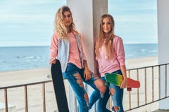 2 красивых девушки в ультрамодных одеждах представляя с скейтбордами около усовика против морского побережья стоковая фотография rf 2 красивых девушки в ультрамодных одеждах представляя с скейтбордами около усовика против морского побережья стоковая фотография rf