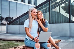 2 красивых девушки сидя владения компьтер-книжка и смотря камеру пока сидящ на стенде на предпосылке стоковые изображения rf 2 красивых девушки сидя владения компьтер-книжка и смотря камеру пока сидящ на стенде на предпосылке стоковые изображения rf