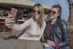2 красивых молодой женщины имея потеху outdoors пока использующ их мобильные телефоны, принимая selfie стоковое фото rf 2 красивых молодой женщины имея потеху outdoors пока использующ их мобильные телефоны, принимая selfie стоковое фото rf