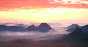 Красная туманная панорама ландшафта в горах Фантастический мечтательный восход солнца на скалистых горах Туманная туманная долина стоковое изображение rf Красная туманная панорама ландшафта в горах Фантастический мечтательный восход солнца на скалистых горах Туманная туманная долина стоковое изображение rf