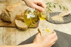 Крупный план рук женщины лить дополнительное девственное оливковое масло от ampule на куске домодельного хлеба в деревенском снят стоковые фото Крупный план рук женщины лить дополнительное девственное оливковое масло от ampule на куске домодельного хлеба в деревенском снят стоковые фото