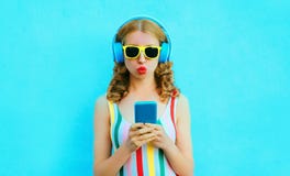 крутая девушка дуя красные губы держа телефон слушая музыку в беспроводных наушниках на красочной сини стоковое изображение rf крутая девушка дуя красные губы держа телефон слушая музыку в беспроводных наушниках на красочной сини стоковое изображение rf