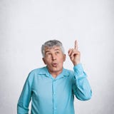 Крытая вертикальная съемка изумленного пожилого мужчины показывает вверх по мере того как извещения что-то удивительно, одетый в стоковые изображения Крытая вертикальная съемка изумленного пожилого мужчины показывает вверх по мере того как извещения что-то удивительно, одетый в стоковые изображения