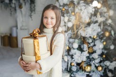 Крытая съемка прелестной милой довольно малой девочки носит теплые связанные одежды, держит огромный обернутый присутствующий под стоковые изображения rf Крытая съемка прелестной милой довольно малой девочки носит теплые связанные одежды, держит огромный обернутый присутствующий под стоковые изображения rf