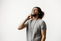 Курчав-головый красивый человек нося серую футболку и сорванные джинсы стоящ и слушающ к музыке в наушниках стоковое фото Курчав-головый красивый человек нося серую футболку и сорванные джинсы стоящ и слушающ к музыке в наушниках стоковое фото